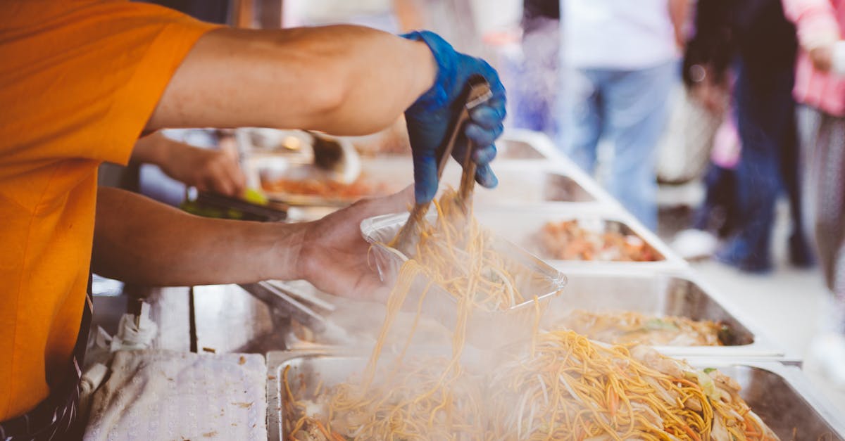 A street vendor serving freshly cooked noodles at a bustling outdoor market.