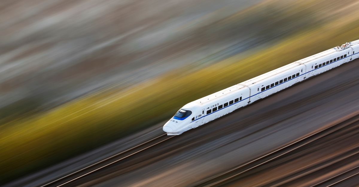 A sleek white high-speed train traveling at top speed, captured with a motion blur effect.