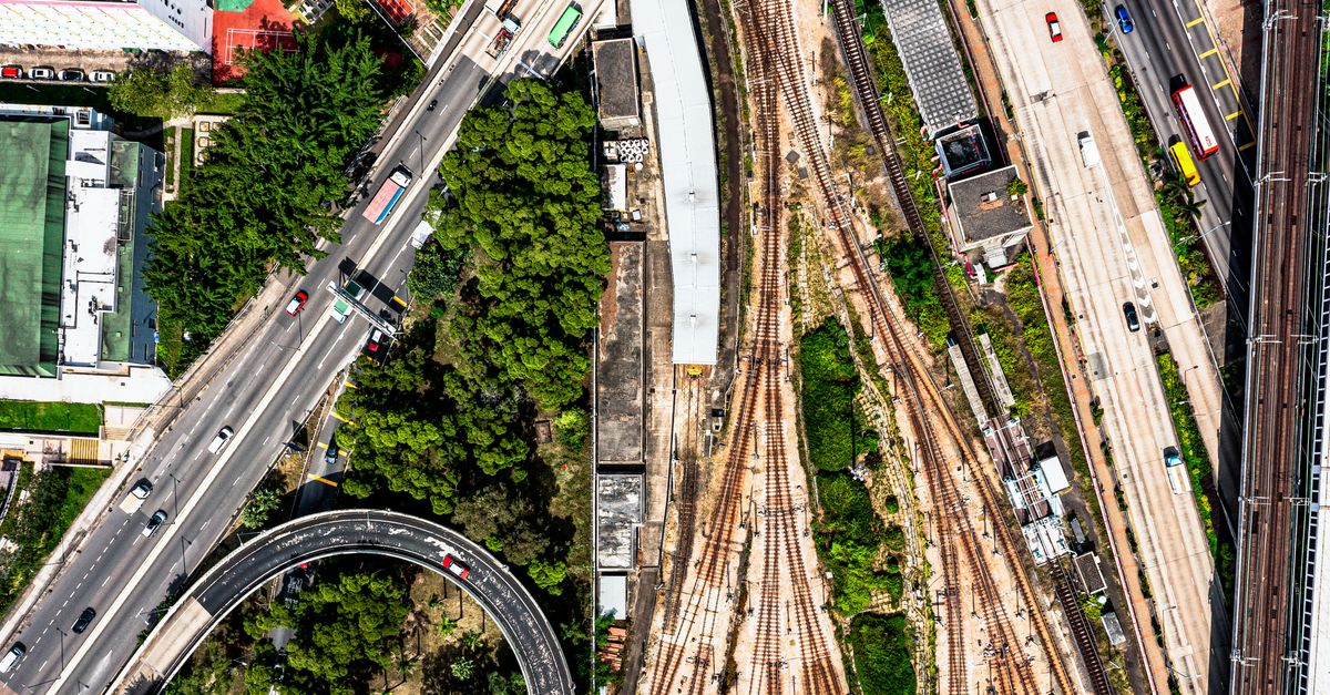 Dynamic aerial shot of Hong Kong's roads, railway tracks, and lush greenery.