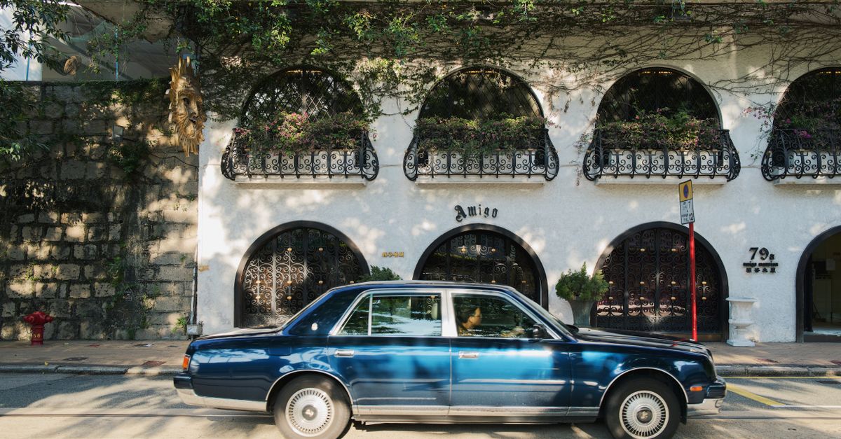 A charming vintage blue sedan parked in front of a Spanish-style building with arched windows.