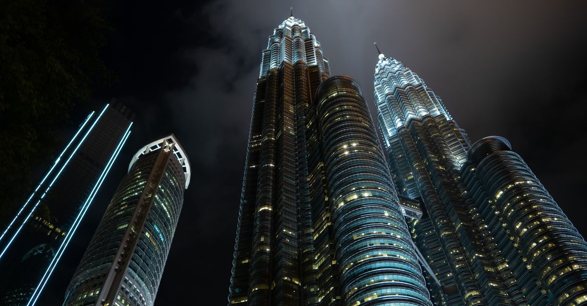 A dramatic low angle shot of the Petronas Twin Towers illuminated against the night sky in Kuala Lumpur, Malaysia.