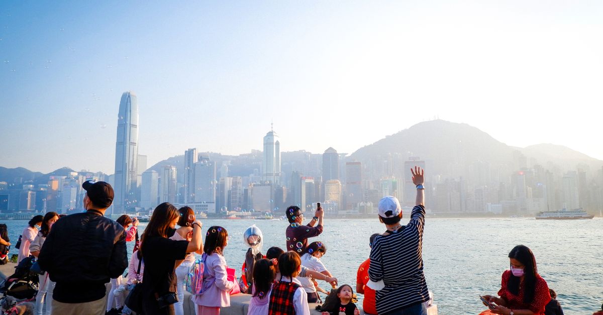 A lively scene of families enjoying a sunny day by the Hong Kong waterfront with city skyline in the background.