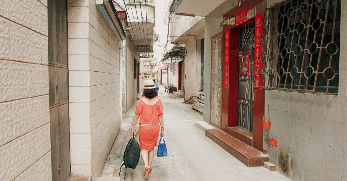 A woman in a stylish outfit strolls through a narrow alley between urban houses.