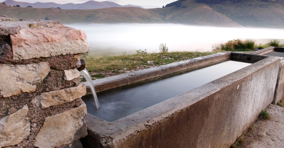 Tranquil mountain valley scene with a rustic stone trough and misty landscape.