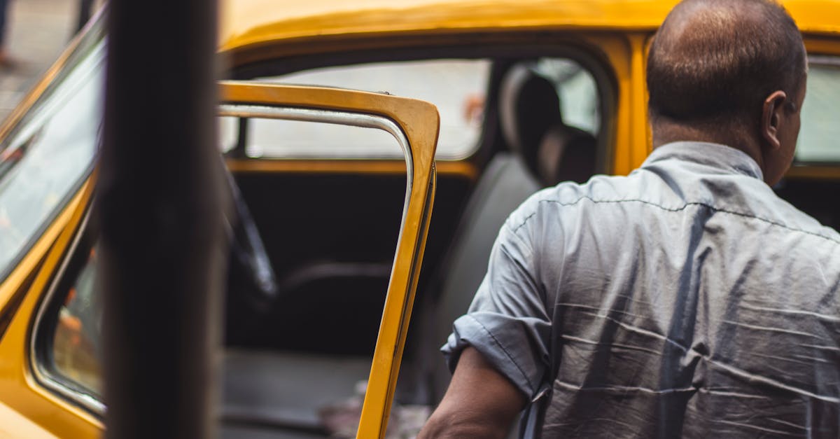Back view of a man opening the door of a parked yellow car.