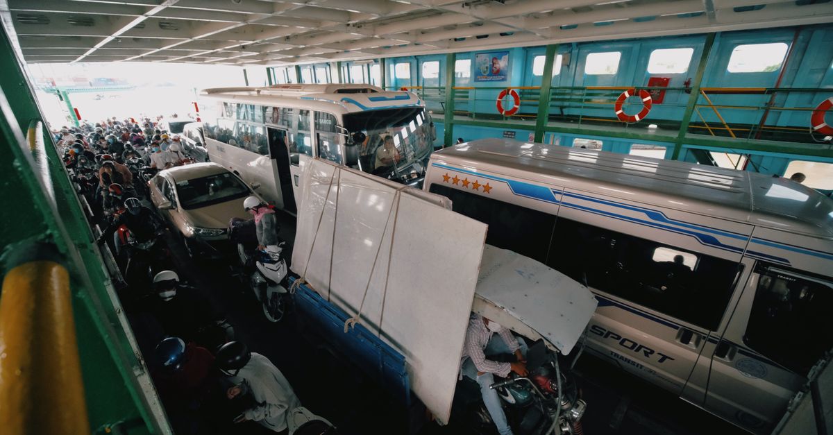 A crowded ferry interior loaded with various vehicles and people, emphasizing urban transport.
