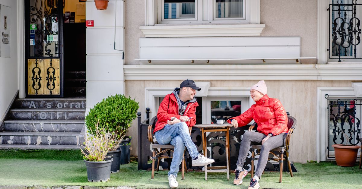A couple conversing outside a hotel café, enjoying a relaxed moment on a sunny day.