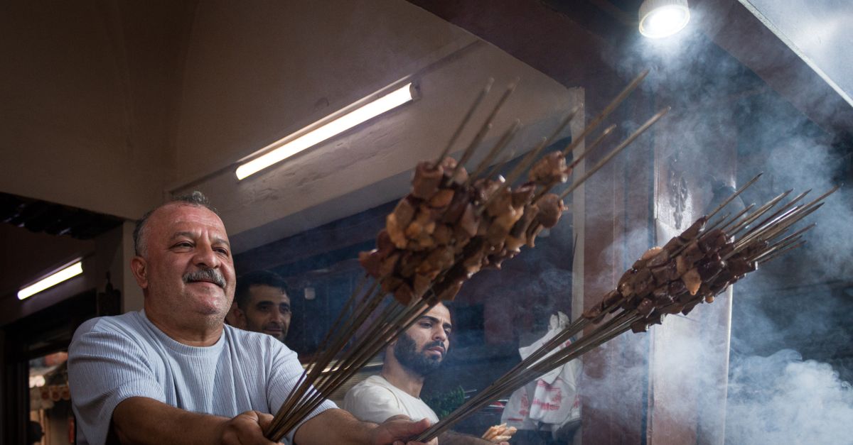 A street food vendor grills skewered meat in a smoky outdoor setting, offering a traditional culinary experience.