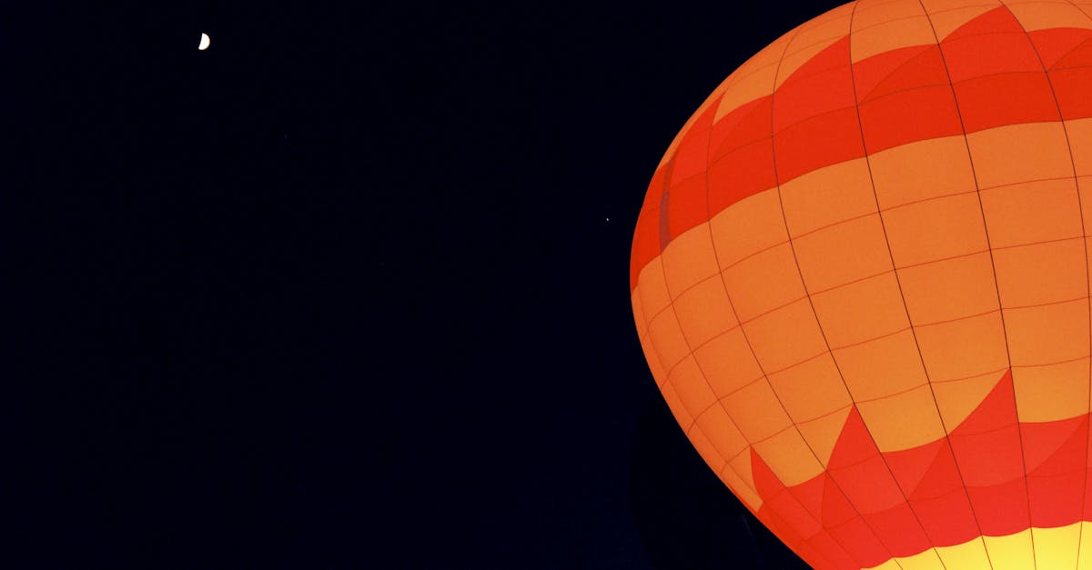 A glowing hot air balloon illuminates the dark night sky next to a crescent moon.