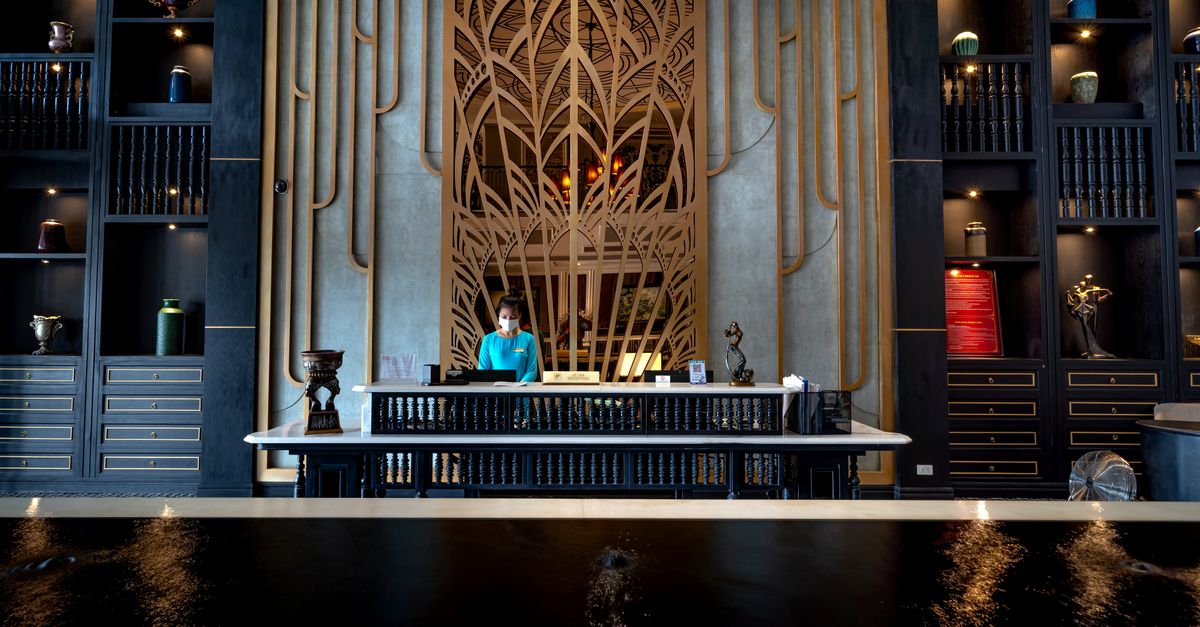 Elegant hotel reception with a modern design, featuring a receptionist at the front desk, ornate decor, and luxury ambiance.