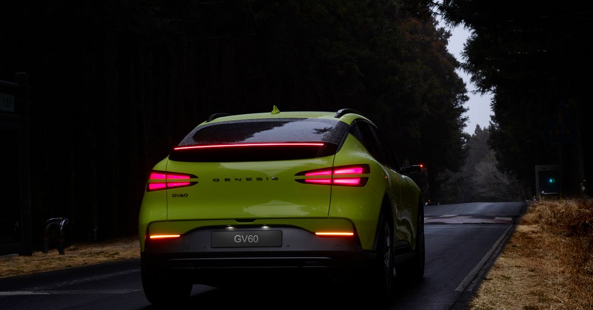 Lime green Genesis GV60 SUV traveling on a dark forest road, captured from behind.