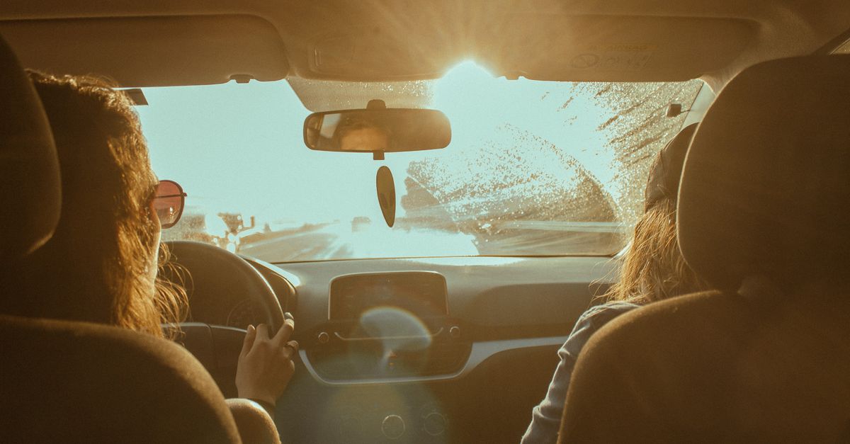 Two women enjoy a road trip with sunlight streaming through the windshield, creating a warm, adventurous scene.