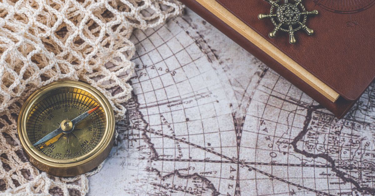 Flat lay of a vintage compass and leather notebook on a retro maritime map.