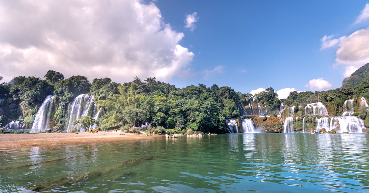 Majestic view of Ban Gioc-Detian Falls with lush greenery and clear waters under a vibrant sky.