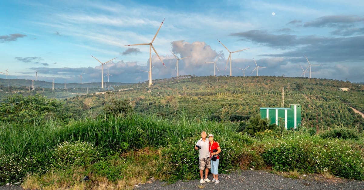 Couple posing in scenic countryside with wind turbines, symbolizing sustainability and renewable energy.