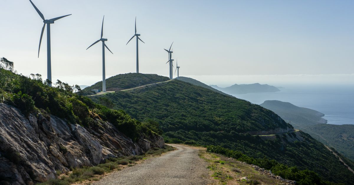 Wind turbines line a coastal mountain road under a clear sky, showcasing renewable energy in nature.