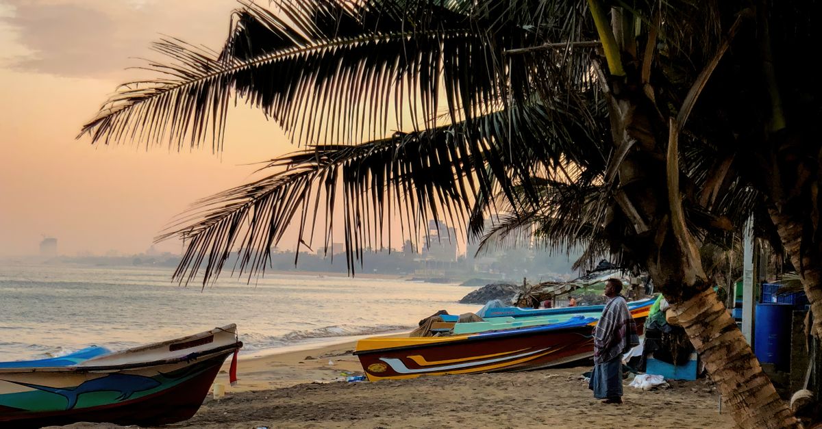 A tranquil beach scene with fishing boats and palm trees at sunset, creating a peaceful atmosphere.