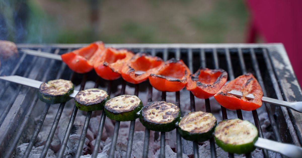 Close-up of grilled vegetables including bell peppers and zucchini on BBQ skewers outdoors.