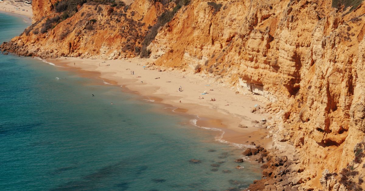 Beautiful Algarve beach with golden cliffs and clear ocean waters, perfect for summer travel.