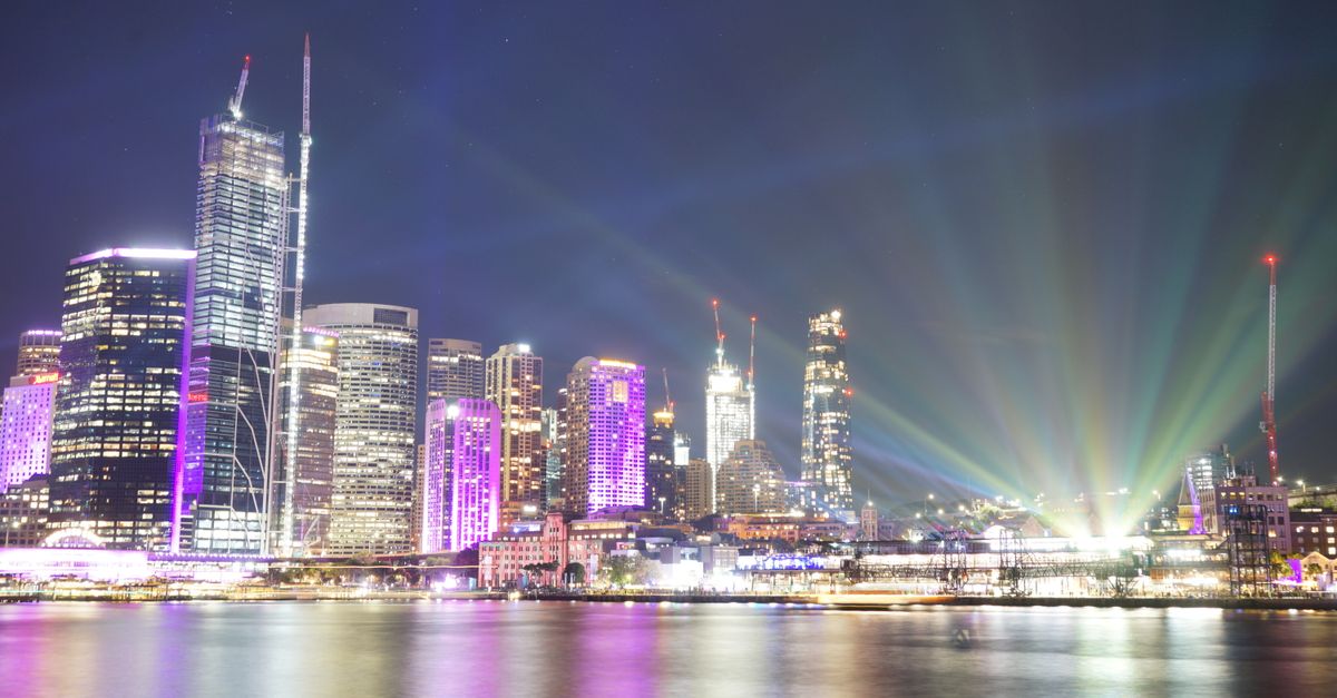 Illuminated Sydney skyline at night showcasing skyscrapers and modern architecture with vibrant lights reflecting on the water.