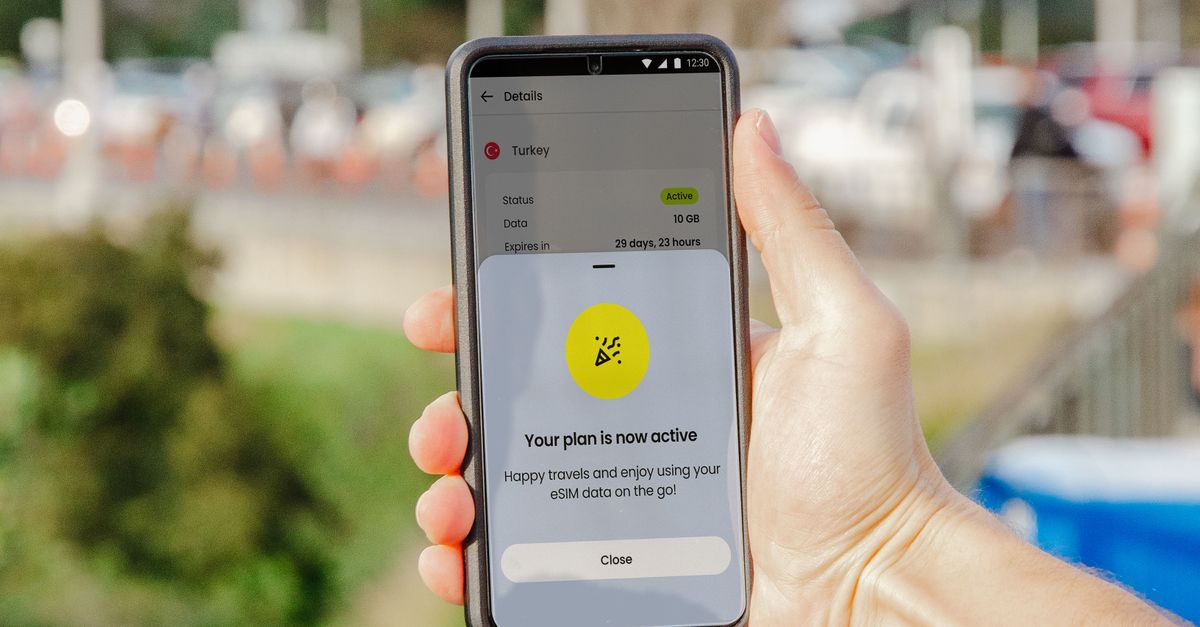 Smartphone showing active eSIM plan held outdoors, blurred city background.