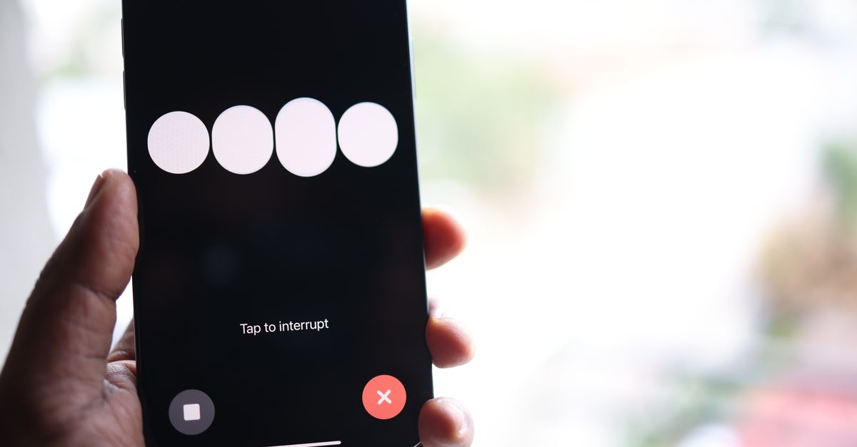 Close-up of a smartphone screen displaying a 'Tap to interrupt' prompt held in a hand.