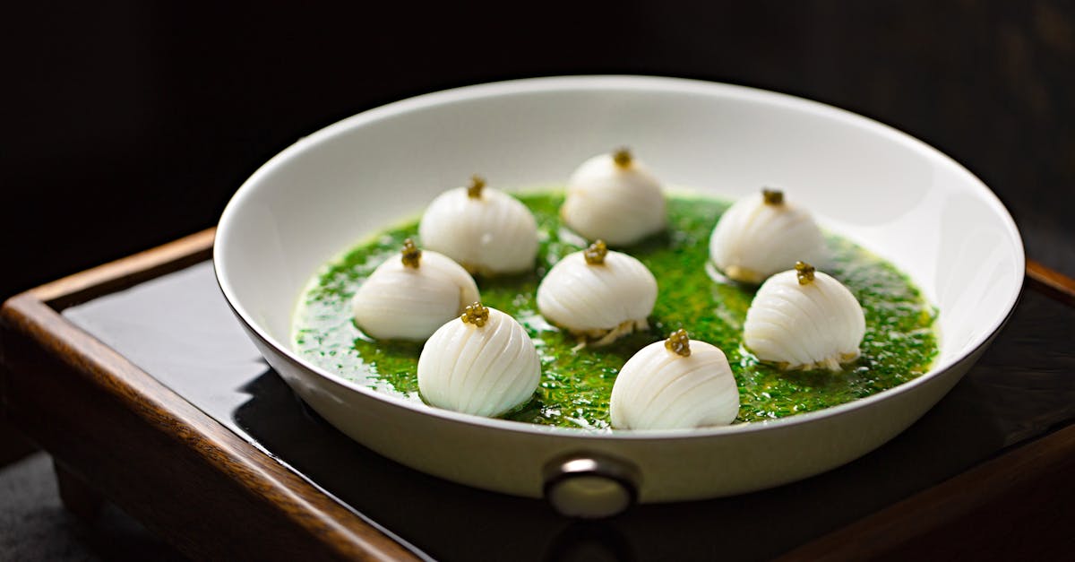 A gourmet dish beautifully presented in a white bowl, featuring white layered spheres on a bed of vibrant green sauce.