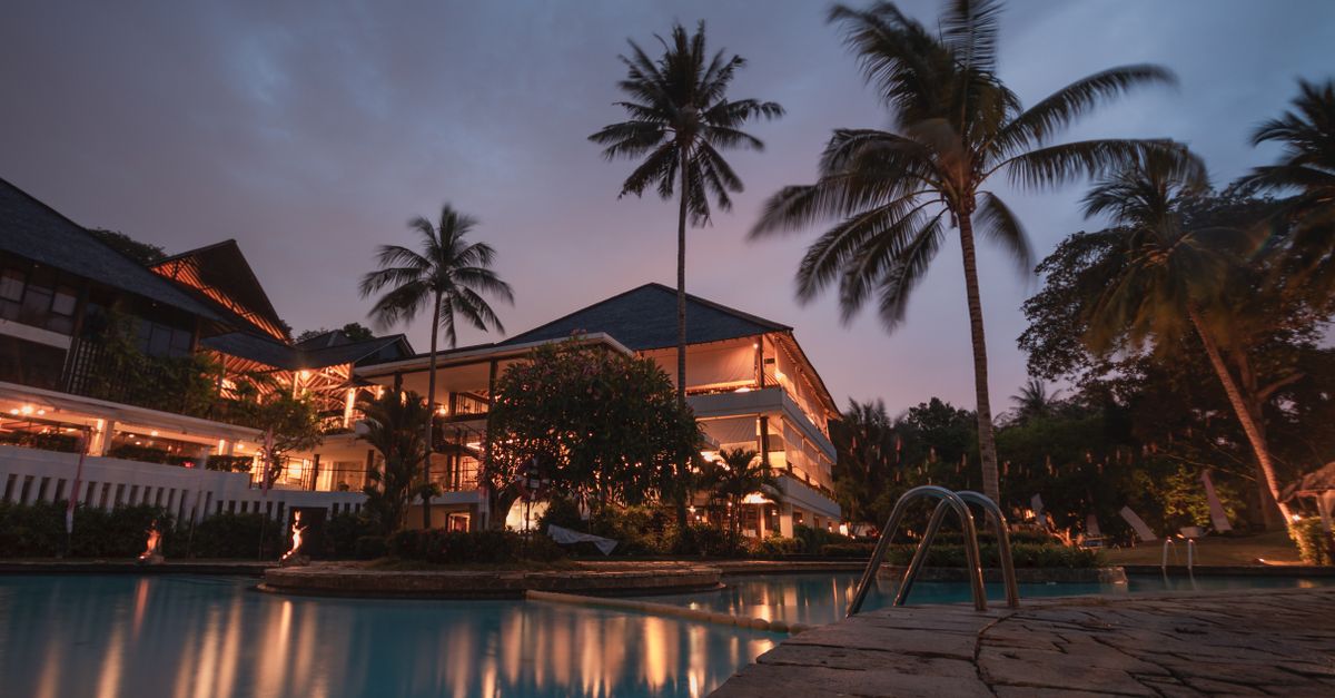 Luxurious tropical resort with swimming pool and palms at dusk, perfect for a tranquil vacation.