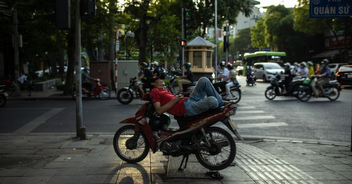 A man takes a nap on his motorcycle amidst the bustling streets of Hanoi, Vietnam.