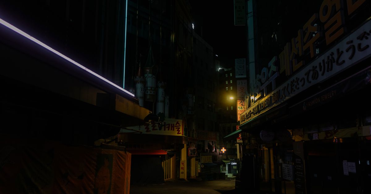 A dimly lit urban alley at night with neon signs and empty streets.