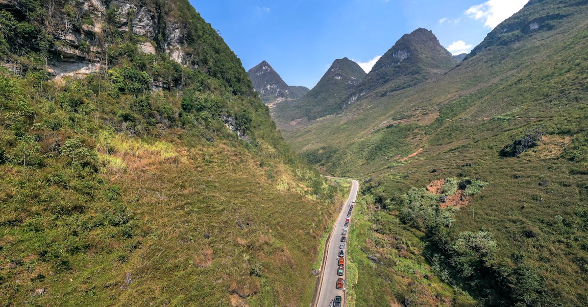 Aerial view of a picturesque mountain road winding through lush green valleys under a clear blue sky.