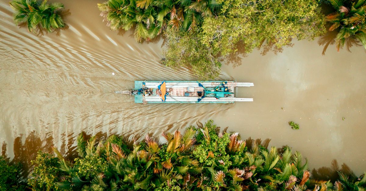 Aerial shot of a boat navigating a river surrounded by lush Vietnamese jungle.