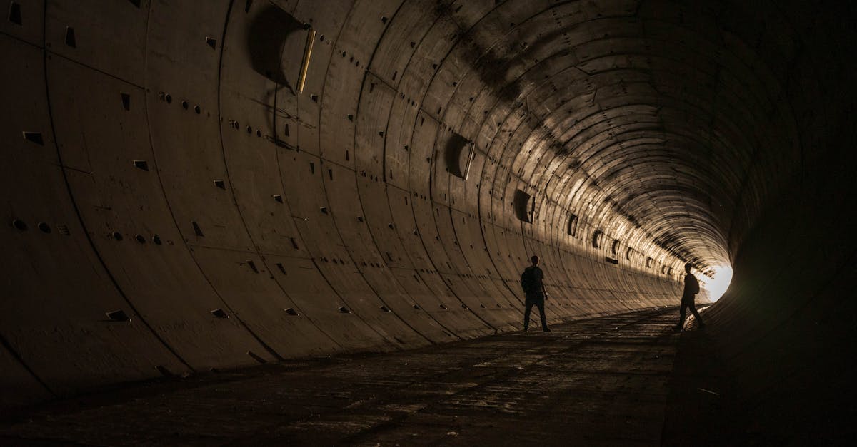 Dramatic silhouettes of two figures standing in an industrial tunnel with light at the end.
