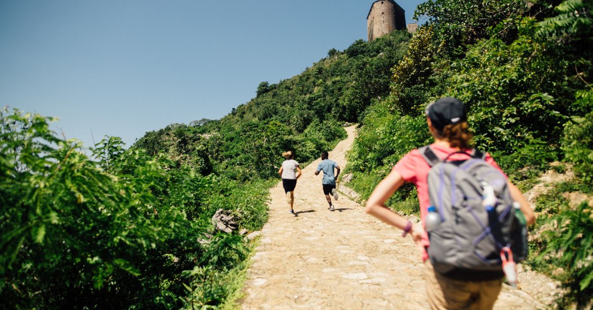 People hiking on a sunny mountain trail with a tower in the background, enjoying nature and leisure.