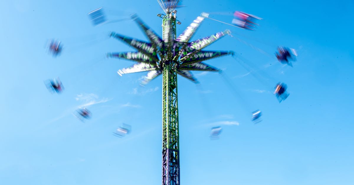 Blurred motion of a towering amusement park ride swinging visitors against a clear blue sky.