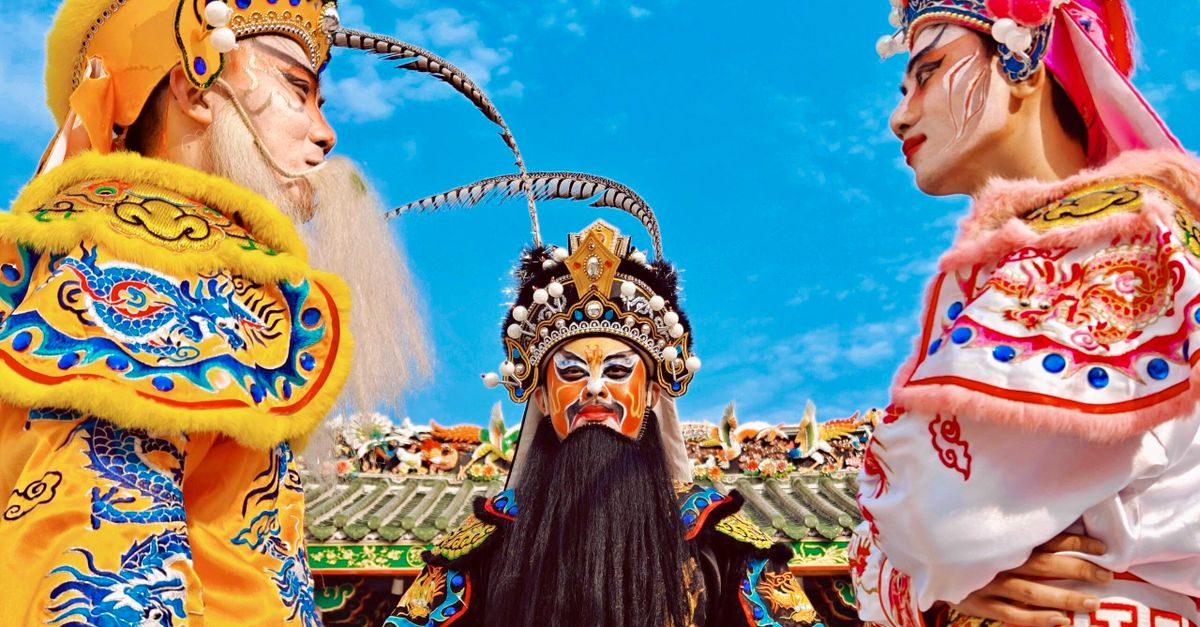 Brightly colored traditional Chinese opera performers in detailed costumes and ornate headpieces against a blue sky.
