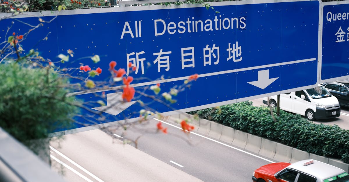 A blue traffic sign in an urban setting directs toward various destinations, with cars below.