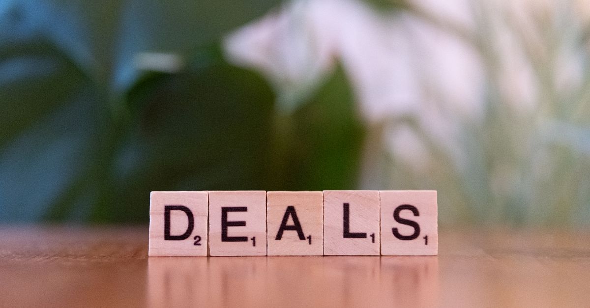 Close-up of Scrabble tiles spelling 'DEALS' on a wooden surface with blurry green background.