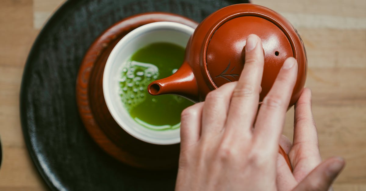 A close-up of hands pouring matcha tea in a Japanese teapot for a traditional ceremony.