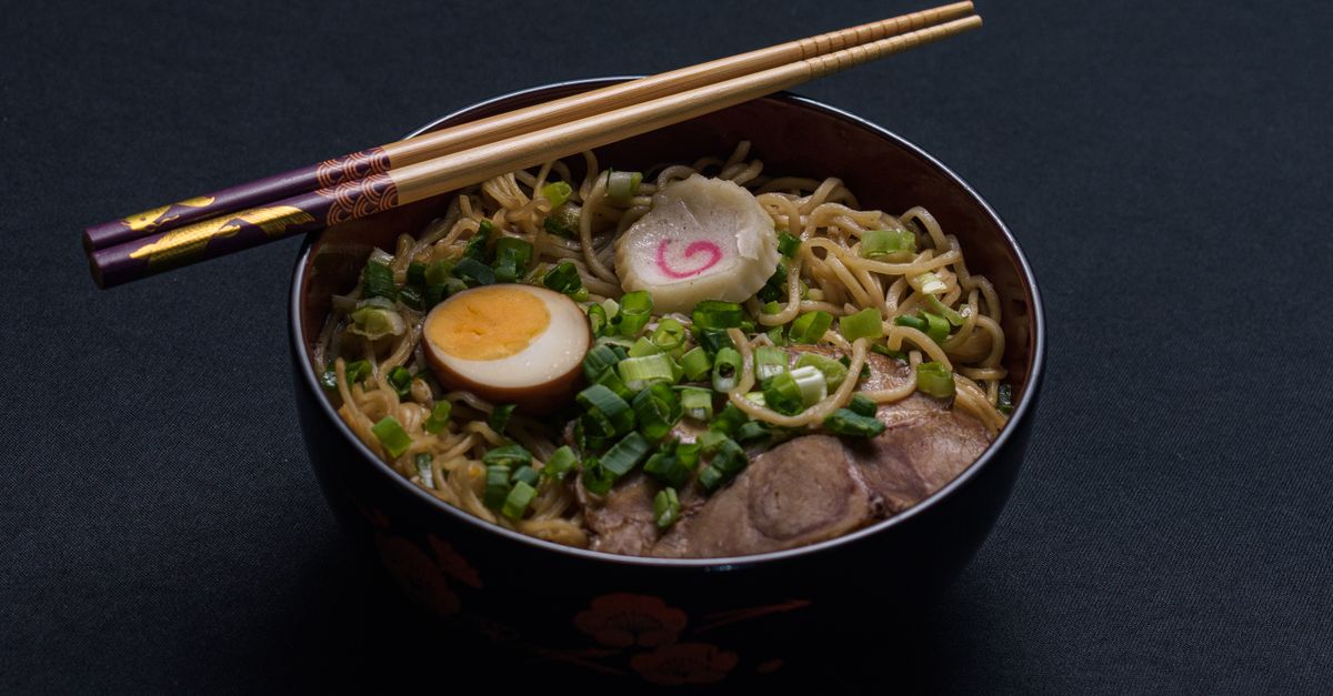 Delicious bowl of Japanese ramen with egg and scallions, topped with chopsticks.