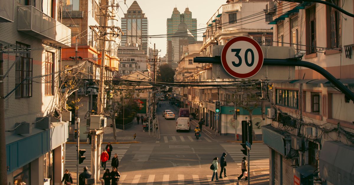 A bustling city street intersection with pedestrians and vehicles under a speed limit sign during daylight.