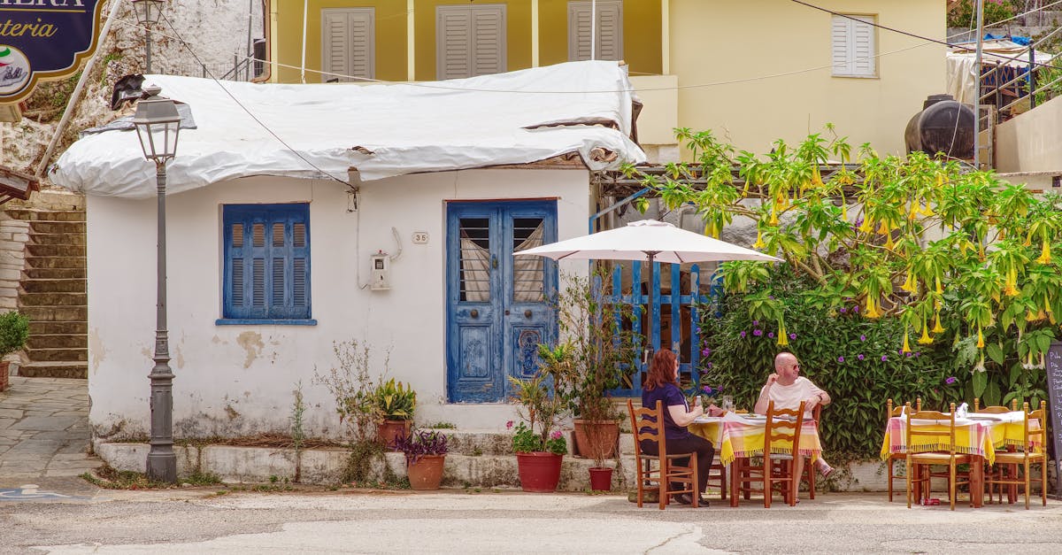 A cozy street-side cafe with people dining under a parasol in Greece.