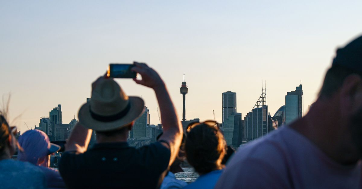 Tourists photograph the Sydney skyline from a boat during sunset. Iconic city view.