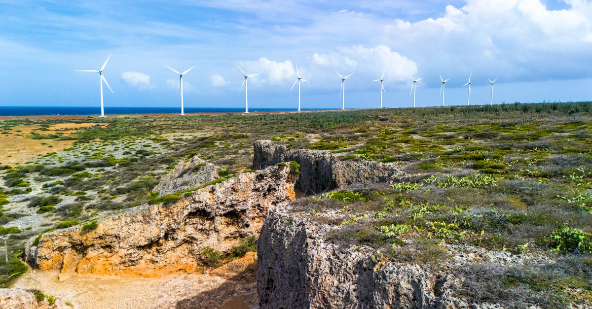 Aerial view of wind turbines along the rocky cliffs of a Caribbean coast with a clear blue sky and ocean.