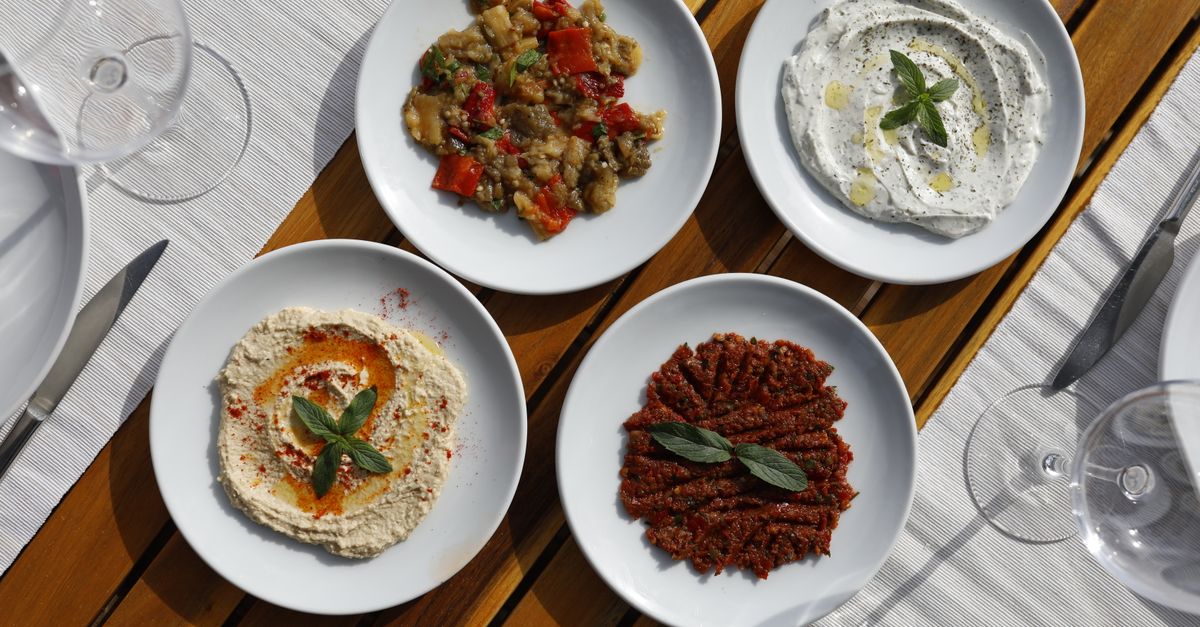 Aerial view of Mediterranean meze with diverse dips on white plates, outdoors.