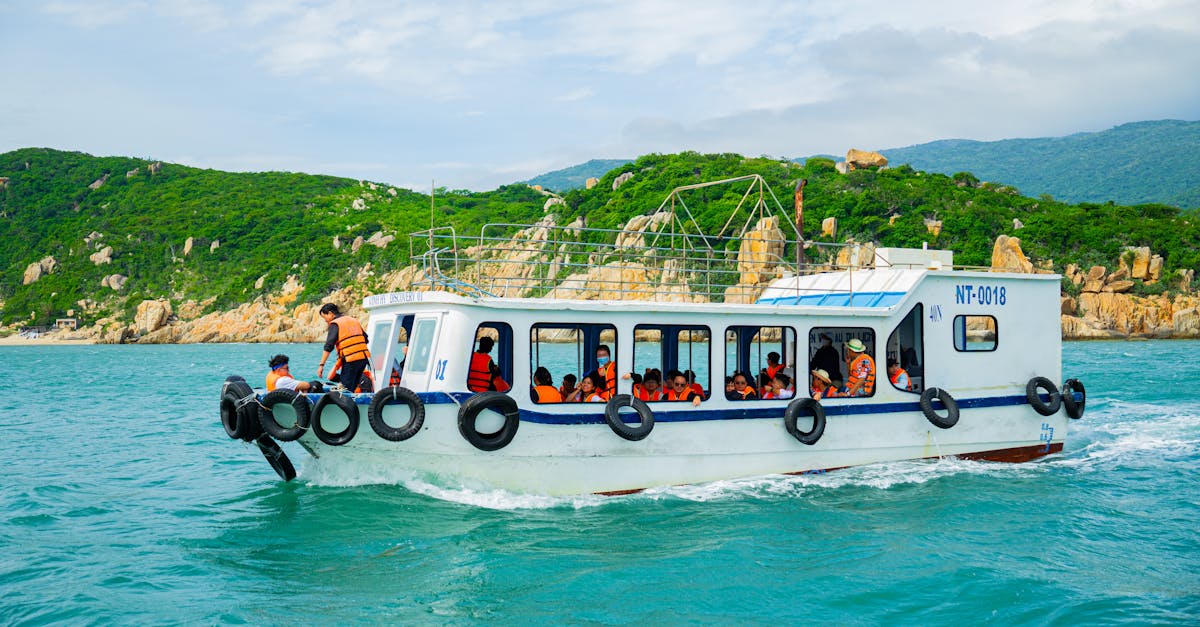 A boat filled with tourists in life jackets traverses vibrant turquoise waters along a lush, green coastline.