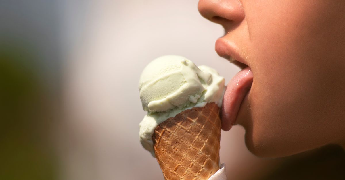 A close-up of a person enjoying a green ice cream cone on a sunny day.