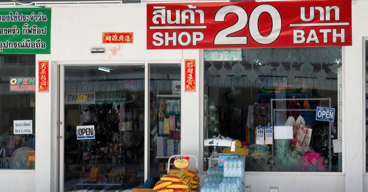 Street view of a budget shop in Thailand with bilingual signage and goods outside.