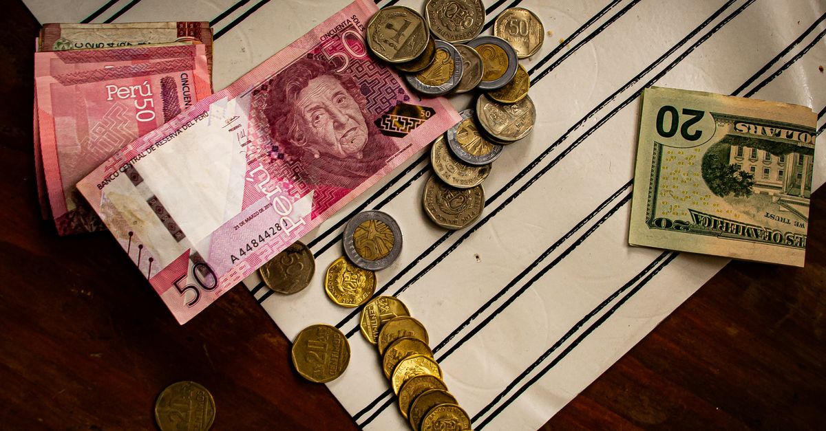 Image of Peruvian banknotes and US dollar bills with scattered coins on a striped surface.