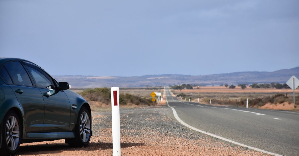A parked car beside an open highway in a vast, serene landscape under a clear sky.